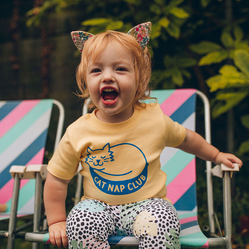 a toddler wears a t-shirt with a sleeping cat and the words 'cat nap club'. She also wears cat ears and roars at the camera, looking like she has no intention of napping...
